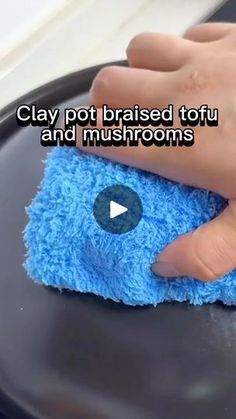 a person cleaning a black plate with a blue cloth on it that says clay pot raised tofu and mushrooms