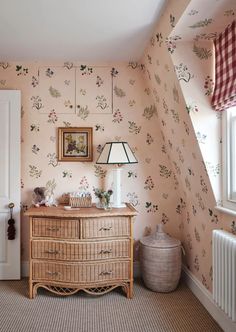 a bedroom with floral wallpaper and a wicker dresser in front of a window