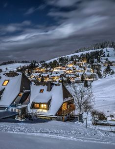 a ski resort at night with snow on the ground and lit up buildings in the background