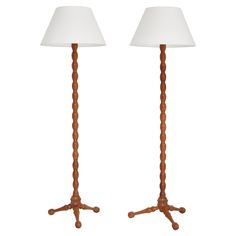 two wooden floor lamps with white shades on them