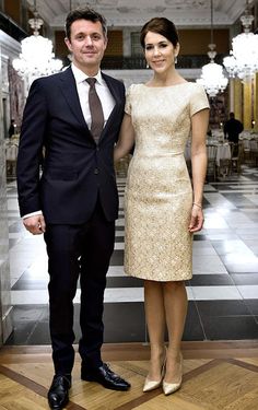 a man and woman standing next to each other in front of a hallway with chandeliers