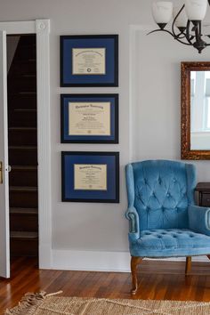 a blue chair sitting in front of a wall with three framed diplomas on it