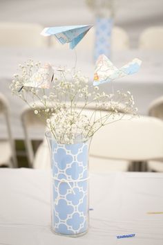 a vase filled with white flowers and paper birds on top of a blue table cloth