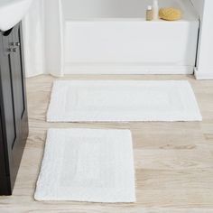 two white bath mats sitting on top of a wooden floor