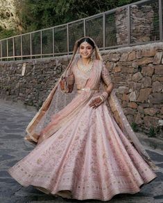 a woman in a pink lehenga is walking down the street with her hand on her hip