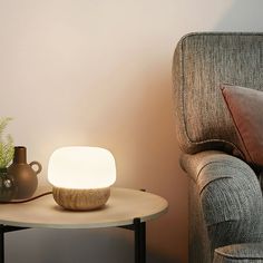 a small table with a lamp on it next to a couch and vases in the corner