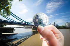 a person holding up a coin in front of a bridge