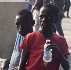 two young boys standing next to each other and one is holding a bottle of water