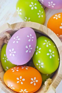 colorful easter eggs in a wooden bowl on a white tablecloth with flowers painted on them