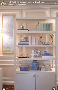 a white book shelf with blue and white dishes on it's shelves in a living room