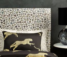 a leopard print bed spread with black and gold pillows on top of the headboard