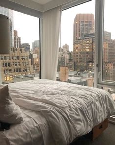 a bed sitting in front of a window next to a large white blanket and pillows