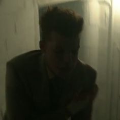 a man in a dark room holding a cell phone and looking at his reflection on the wall