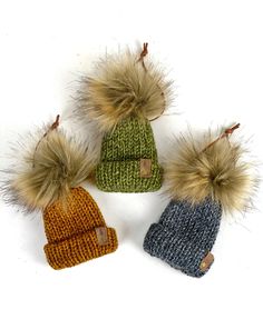 three knitted hats with fur pom - poms on them, all in different colors