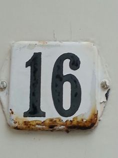 an old rusted sign with the number sixteen written on it is attached to a wall