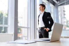 a man standing in front of a laptop computer on a table with his hands behind his back