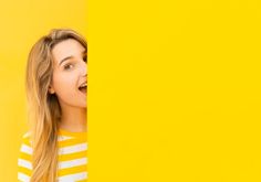 a young woman peeking out from behind a yellow wall with her mouth open and tongue hanging out