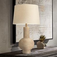 a white lamp sitting on top of a wooden table next to a framed piece of art