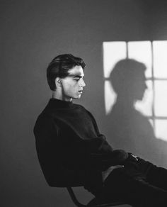 a man sitting in a chair next to a window with the shadow of a person's head