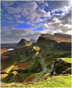 a winding road in the middle of mountains with green grass and flowers on both sides