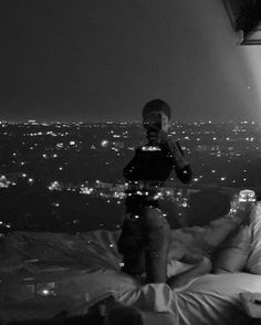 a man taking a photo of himself in bed at night with the city lights behind him