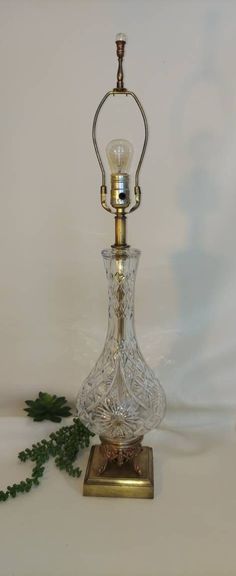 a glass lamp with a metal base on a white tableclothed surface next to a green plant