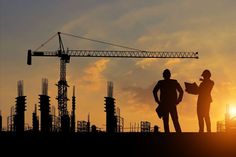 two people standing in front of a construction site with the sun setting behind them,