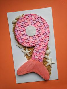 a pink and white paper with a fish on it's tail, surrounded by sea shells