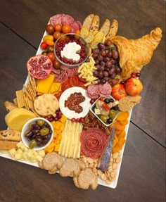 a platter filled with cheese, crackers, meats and fruit on a wooden table