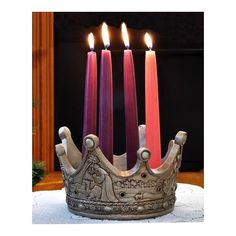 four candles are lit in a crown shaped candle holder on top of a white table