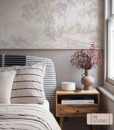 a bed sitting next to a window with a vase filled with flowers on top of it