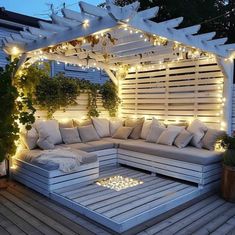 a white couch sitting under a pergoline covered with lights and pillows on top of a wooden deck