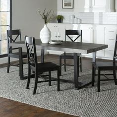 a dining room table with four chairs and a vase on the floor in front of it