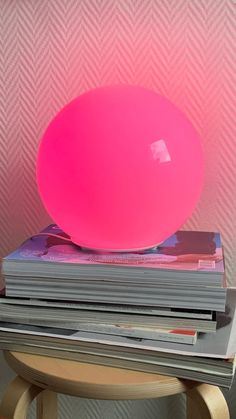 a pink ball sitting on top of stack of magazines in front of a pink wall