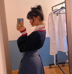 a woman taking a selfie in front of a mirror while wearing a skirt and sweater