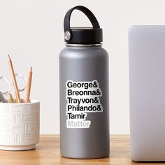 a gray water bottle sitting next to a white laptop computer on a wooden desk with a sticker that says stay home