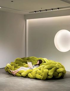 a woman laying on top of a green bean bag chair next to a white wall