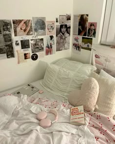 a white bed topped with lots of pillows next to a wall covered in pictures and photos