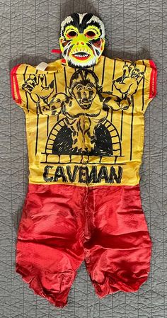 a yellow shirt and red shorts with an image of a demon on the chest, in front of a gray background