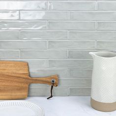 a white vase sitting on top of a counter next to a cutting board and plate