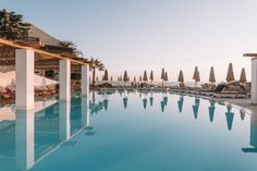 an outdoor pool with lounge chairs and umbrellas next to the water at sunset or dawn