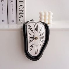 a black and white clock sitting on top of a book shelf next to some books