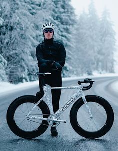 a man is standing next to his bike on the side of the road in the snow