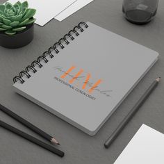 a spiral notebook with the initials h and w on it next to pencils, paper towels and a potted plant