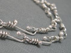 two silver necklaces on a gray surface with one chain attached to the clasp and another link at the end