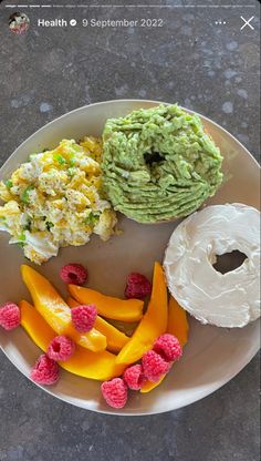 a white plate topped with fruit and a bagel covered in guacamole