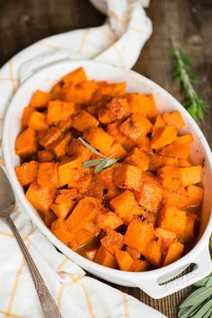 a white dish filled with sweet potatoes on top of a table next to a spoon