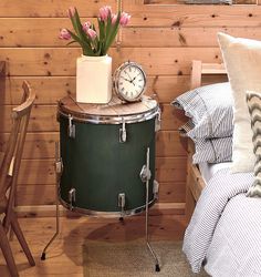 a green drum sits next to a small table with a clock on it and flowers in a vase