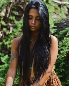 a woman with long black hair sitting in the grass