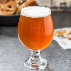 a glass filled with beer sitting on top of a table next to pretzels